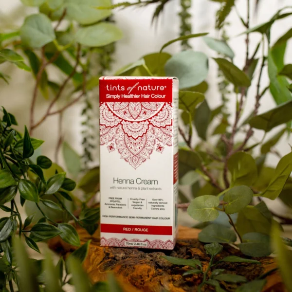 En æske Tints of Nature Henna Cream Red - 70 ml siddende oven på en naturlig plante, fremmer velvære og helbred.